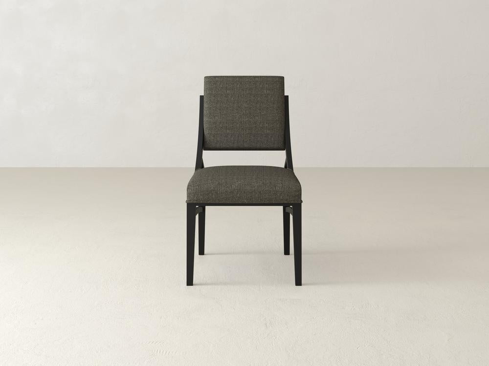 A single, modern dining chair with a dark wooden frame and gray cushioned seat and backrest sits on a light-colored, seamless floor against a plain, off-white wall.