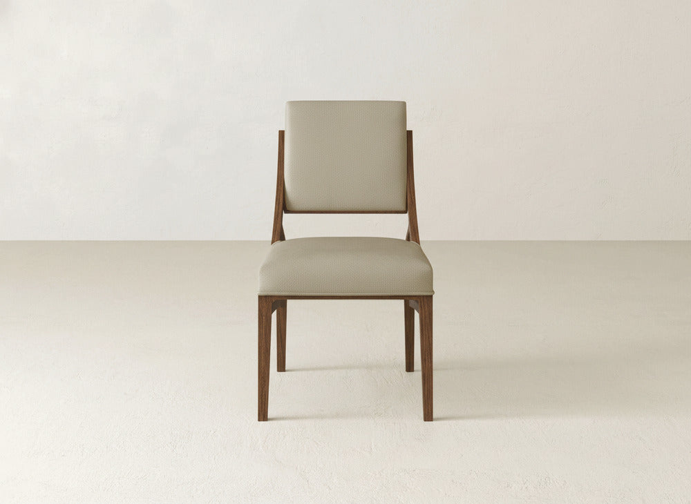 The James+James Quinn Dining Chair features a modern design with a light beige cushioned seat and backrest, clean lines, and no armrests. Ideal for elevating your dining room, it’s set against a plain off-white background.
