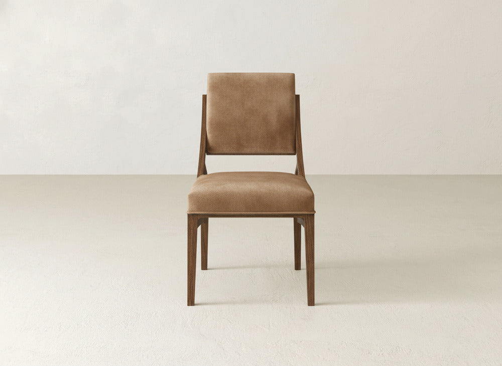 The James+James Quinn Dining Chair features brown upholstery and a sturdy wooden frame, shown from the front on a light floor against an off-white wall—ideal for enhancing your dining room decor.