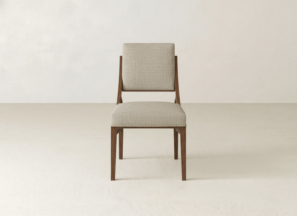 The James+James Quinn Dining Chair features a light beige upholstered seat and backrest, centered on a plain, light floor against an off-white wall—an ideal choice for minimalistic dining room decor.