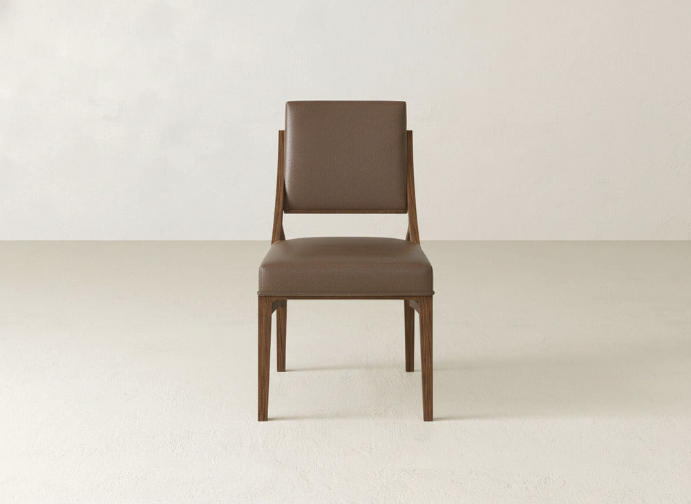 The Quinn Dining Chair by James+James features a brown wooden frame with upholstered padded seat and backrest, shown front-facing against a light wall and floor—ideal for enhancing your dining room decor.