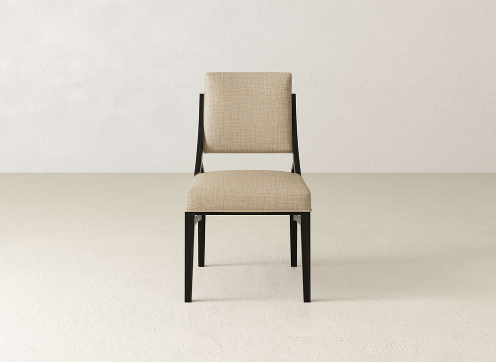 The Quinn Dining Chair by James+James features beige upholstery and a black wooden frame, displayed on a light textured floor with an off-white wall—an ideal choice for modern dining room decor.