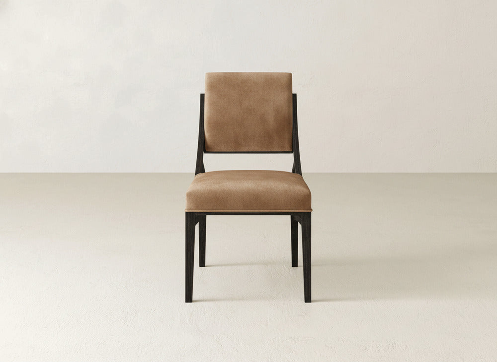 The Quinn Dining Chair by James+James features modern brown upholstery and a black wooden frame, ideal for enhancing your dining space. Shown on a light floor with an off-white wall, it brings stylish comfort to your home.