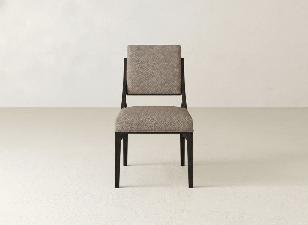 The James+James Quinn Dining Chair features a dark wood frame and light textured upholstery, making it a modern, upholstered dining chair that sits elegantly in a minimal room with light walls and floors.