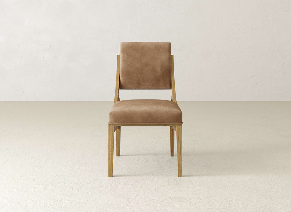 The Quinn Dining Chair by James+James features a light wood frame with tan upholstered seat and backrest, ideal for upgrading your dining room. Shown on a light floor with an off-white wall.