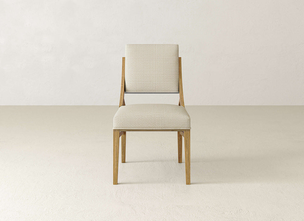 The Quinn Dining Chair by James+James features a light upholstered seat and backrest, ideal for dining rooms. Shown on a plain light floor with an off-white wall for a simple, modern look.