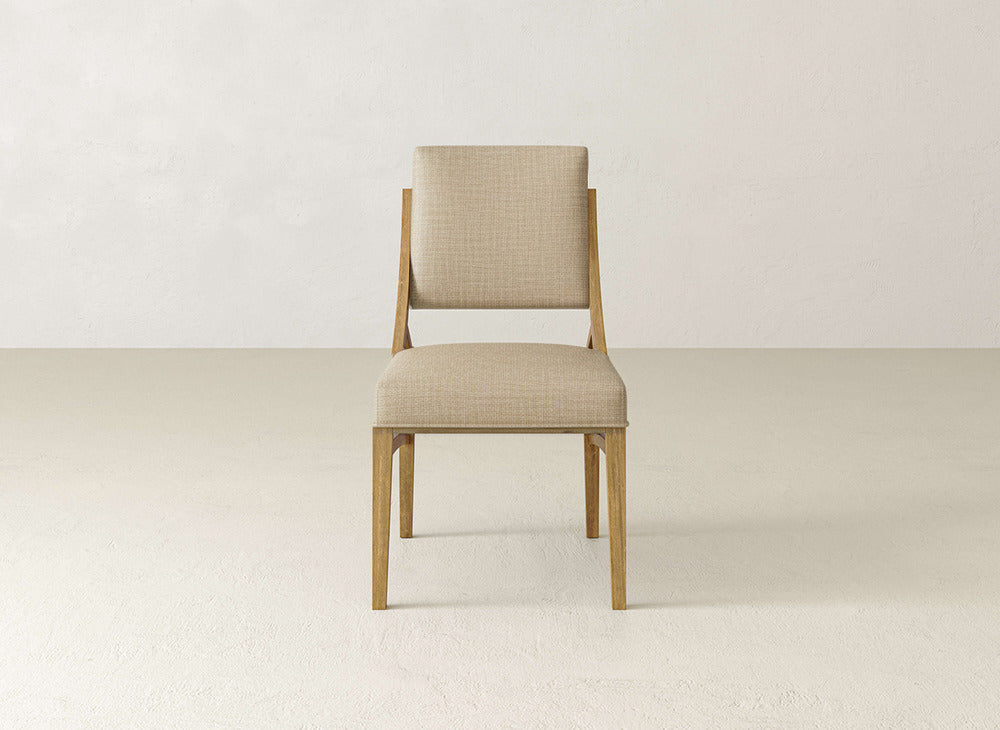 The James+James Quinn Dining Chair, featuring a beige upholstered seat and backrest, is centered and facing forward against a plain light wall and floor—a sophisticated option for elegant dining room decor.