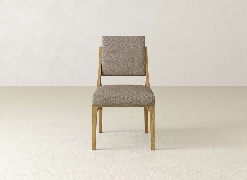 The James+James Quinn Dining Chair features light brown legs and a textured beige upholstered seat and backrest, making it a stylish choice for minimalist dining rooms with off-white walls and floors.