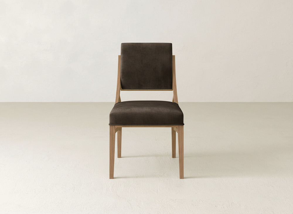 The James+James Quinn Dining Chair, featuring a dark upholstered seat and backrest, stands in a bright room and serves as an elegant focal point for minimalist dining décor.
