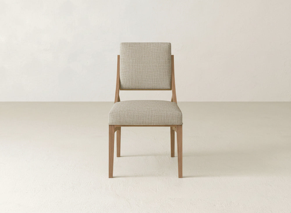 The Quinn Dining Chair by James+James features a light gray upholstered seat and backrest. Its minimalist design is ideal for modern dining rooms, shown here on a light floor against a neutral wall.