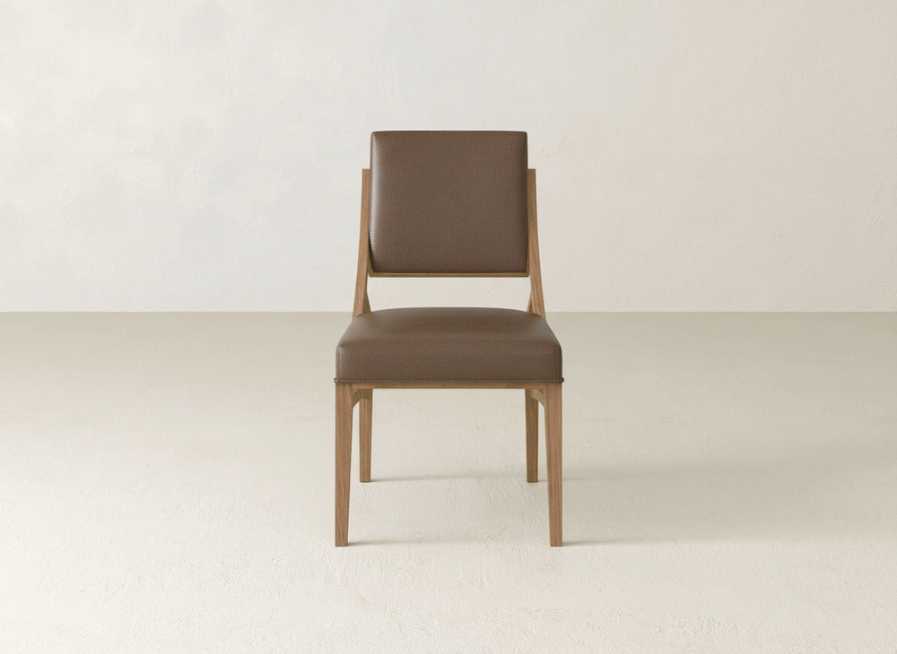 The James+James Quinn Dining Chair features a brown cushioned seat and backrest, set against a plain light wall—a stylish, minimalist option for your dining room.