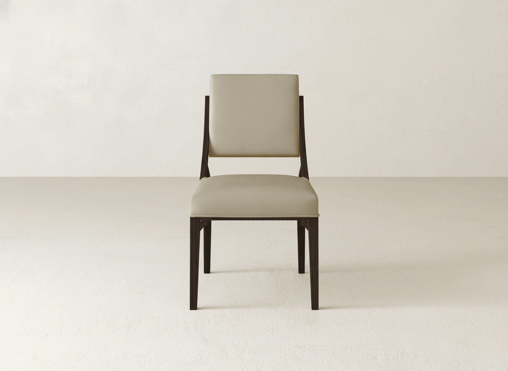 The Quinn Dining Chair by James+James features a beige upholstered seat and backrest with dark wooden legs and frame, standing elegantly in a light, minimalist room—perfect for refined dining room decor.