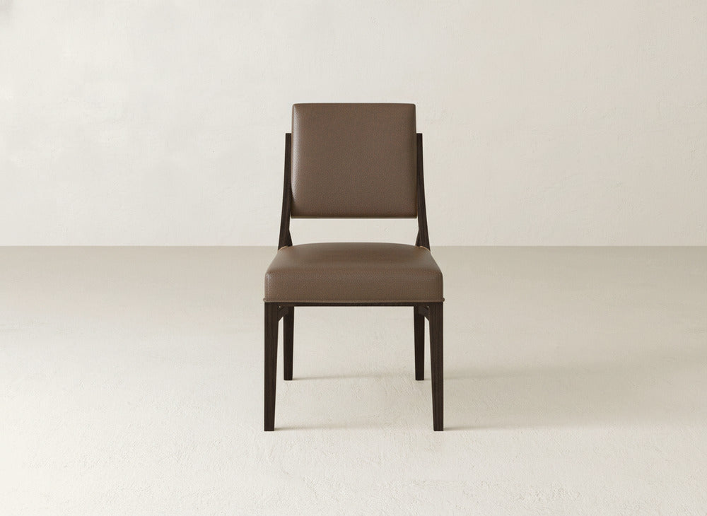 The Quinn Dining Chair by James+James, featuring a brown upholstered seat, cushioned backrest, and dark wooden legs, is centered in a light minimalist room—an ideal choice for modern dining room decor.