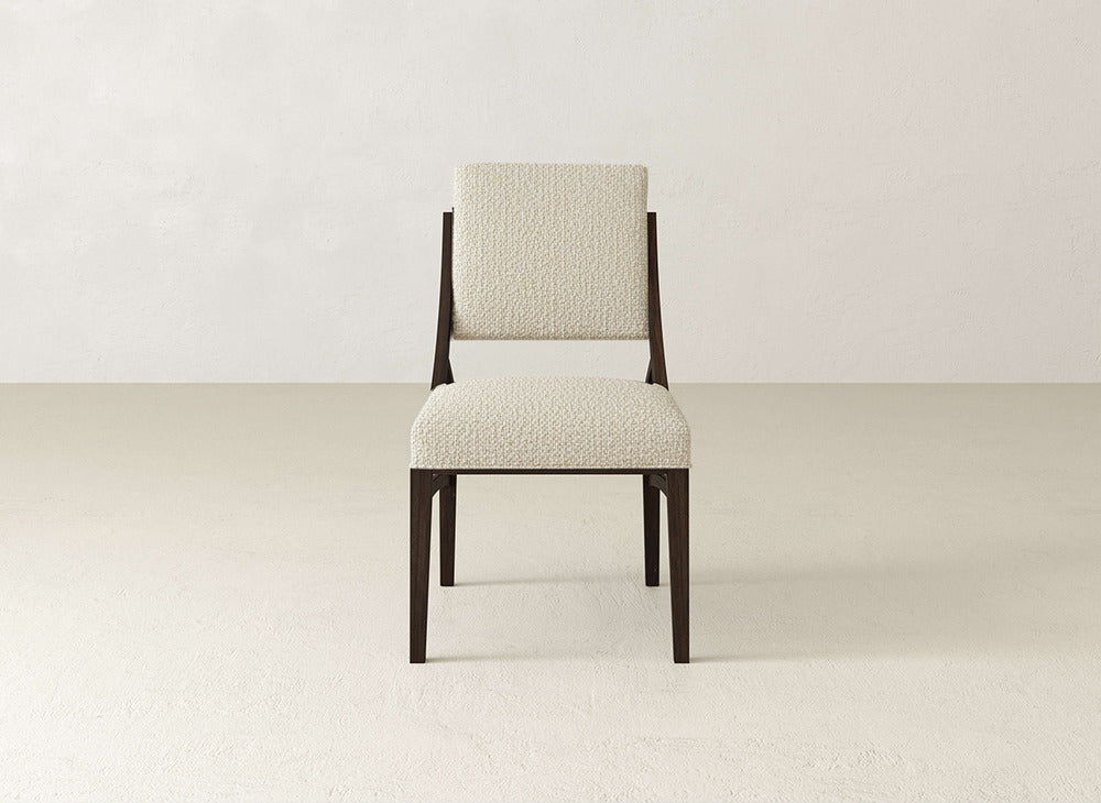 The James+James Quinn Dining Chair features dark wooden legs and a white textured upholstered seat and backrest, ideal for dining rooms with minimal, neutral-toned decor, set against a plain wall and floor.