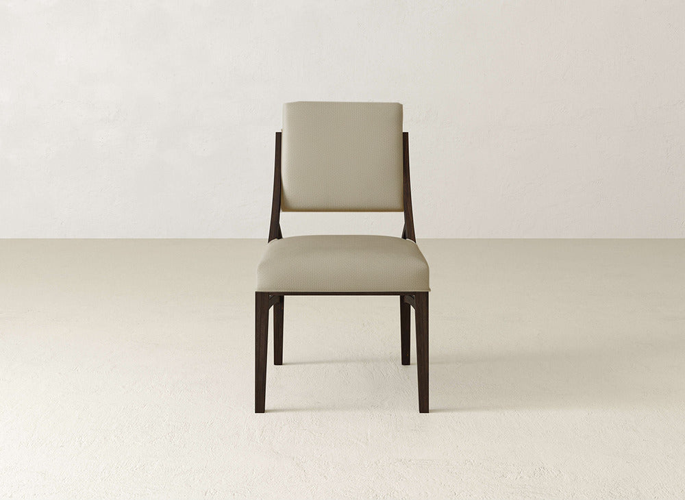 The James+James Quinn Dining Chair features a dark wooden frame and light beige upholstered seat and backrest, ideal for enhancing your dining room. Shown on a light floor against an off-white wall.