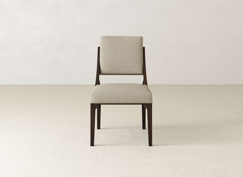 The Quinn Dining Chair by James+James features dark wooden legs, a cushioned seat and backrest in light beige fabric, and adds elegance to any dining room decor against a neutral wall and floor.
