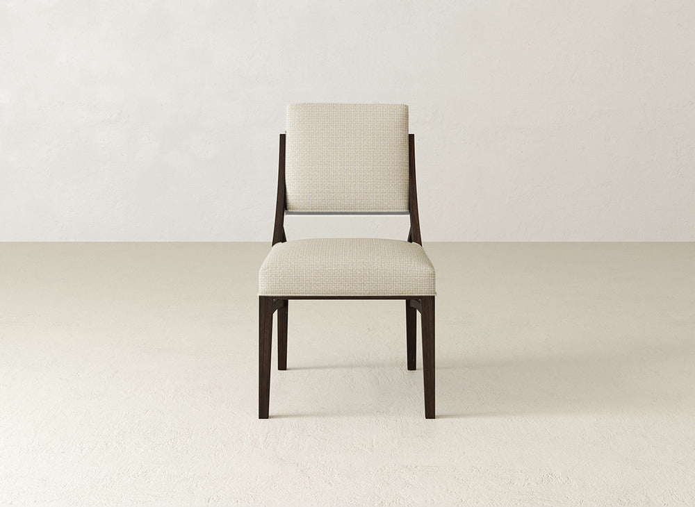 The James+James Quinn Dining Chair features dark wood legs and a light, textured upholstered seat and backrest, ideal for elevating dining spaces. It is shown against a simple, light-colored wall and floor.