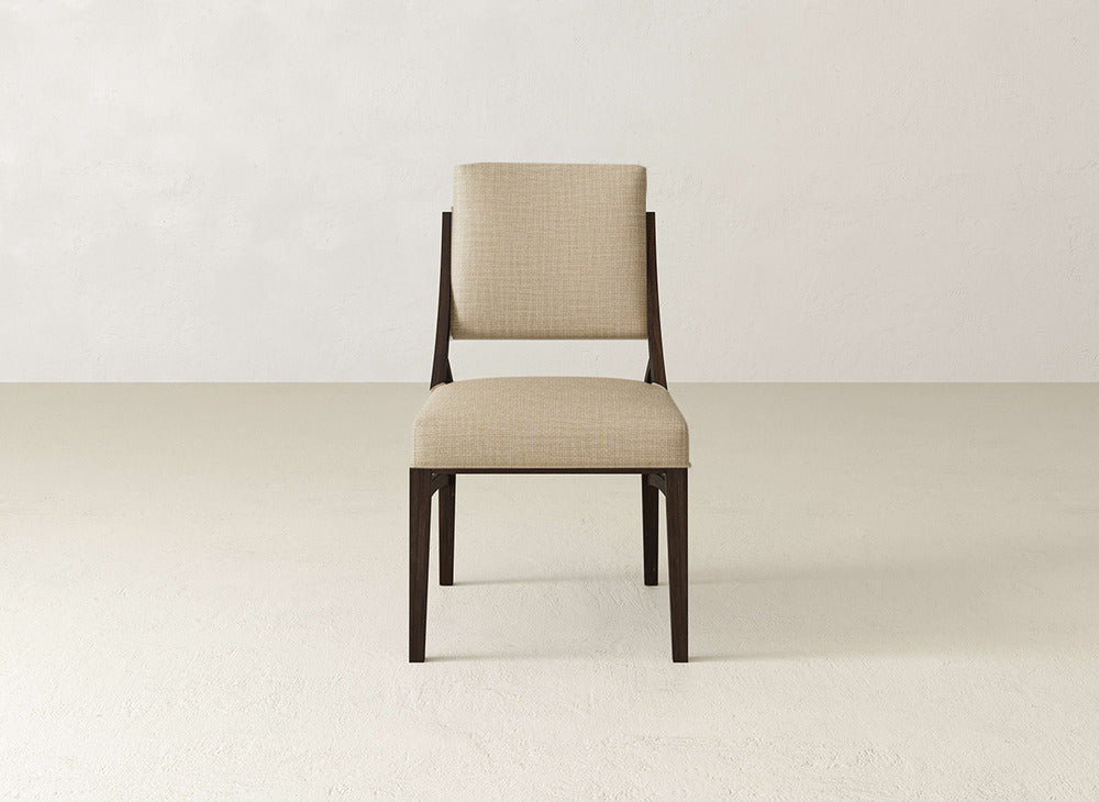 The Quinn Dining Chair by James+James features a modern dark wooden frame with a light beige upholstered seat and backrest, ideal for enhancing your dining room decor. It stands out beautifully on a light floor against an off-white wall.