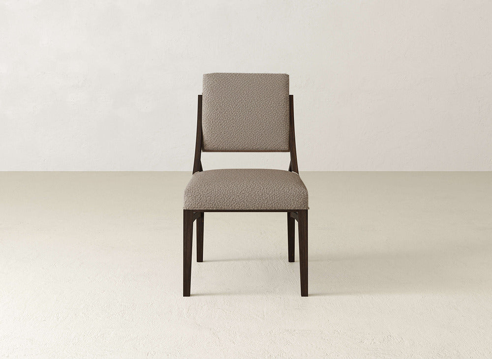 The James+James Quinn Dining Chair pairs a dark wood frame with light beige upholstery on the seat and back, adding style to any dining room. Shown against plain, light walls and flooring for a modern look.