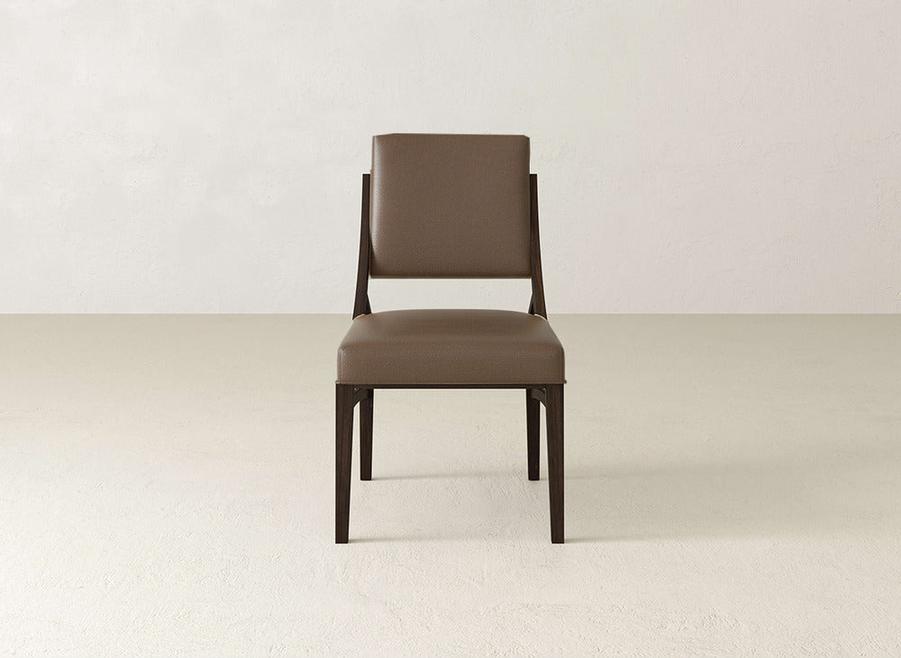 The Quinn Dining Chair by James+James is a modern brown upholstered chair with padded seat and backrest, set on dark straight wooden legs—ideal for dining rooms, as shown on a light floor against a white wall.