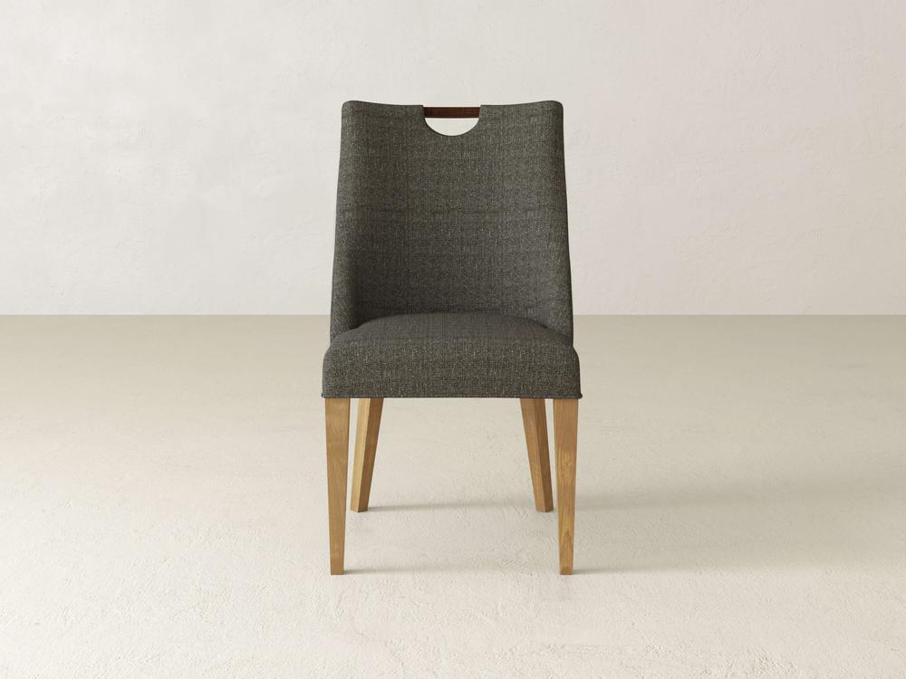 Introducing the Rosalie Dining Chair by James & James, a modern elegant piece with a dark gray cushioned seat and backrest, light wooden legs, and a small cutout handle at the top. Perfect for any dining setting against a plain white backdrop.