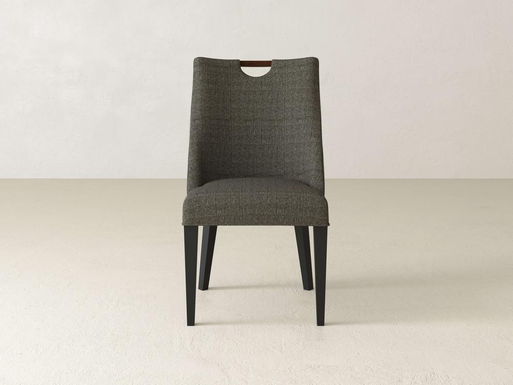 The Rosalie Dining Chair, by James & James, exudes modern elegance with its grey upholstered seat and back, highlighted by a wooden handle at the top. It is supported by four black legs and is showcased against a white background.