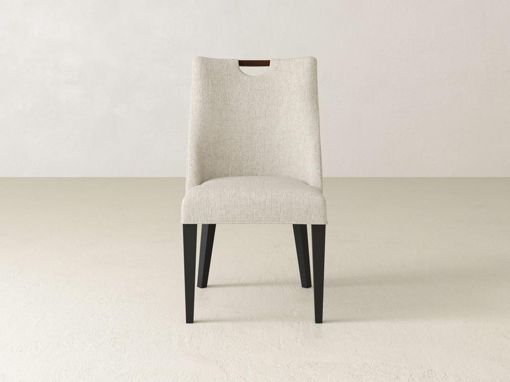 The James & James Rosalie Dining Chair, exemplifying modern elegance, includes a beige upholstered seat with practical design touches like a wooden handle and dark wooden legs, set against a plain white background.