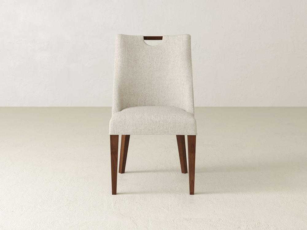 The Rosalie Dining Chair by James & James, with beige fabric and wooden legs, exudes modern elegance. It features a slightly curved backrest that adds sophistication to your dining space, standing gracefully on light floors against neutral walls.