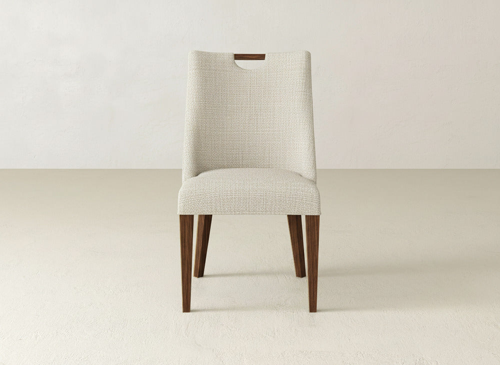 The James & James Rosalie Dining Chair showcases textured off-white upholstery, a rectangular cutout on the backrest, and four wooden legs, creating an elegant, minimalist look.