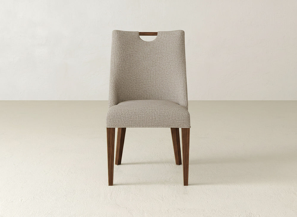 The Rosalie Dining Chair by James & James features beige upholstery, a gently curved back with a top cutout, and four angled wooden legs, shown against a plain light background.