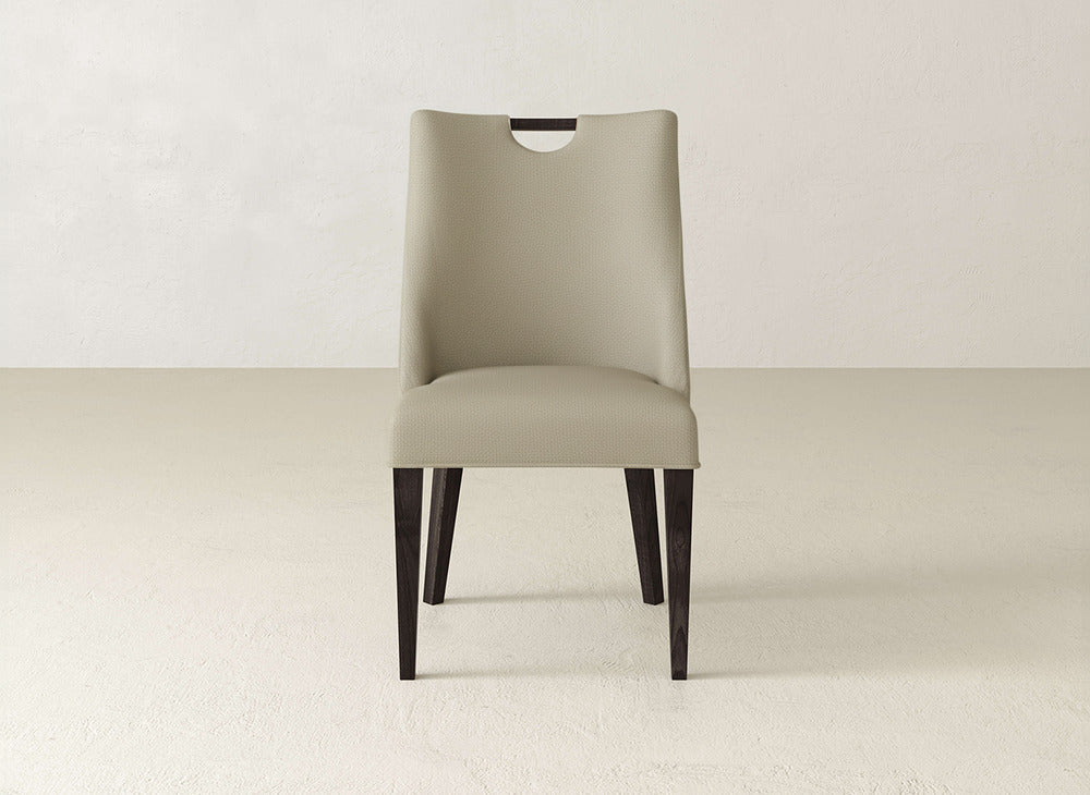 The James & James Rosalie Dining Chair features beige upholstery and dark wooden legs, shown facing forward against a light wall and floor background.