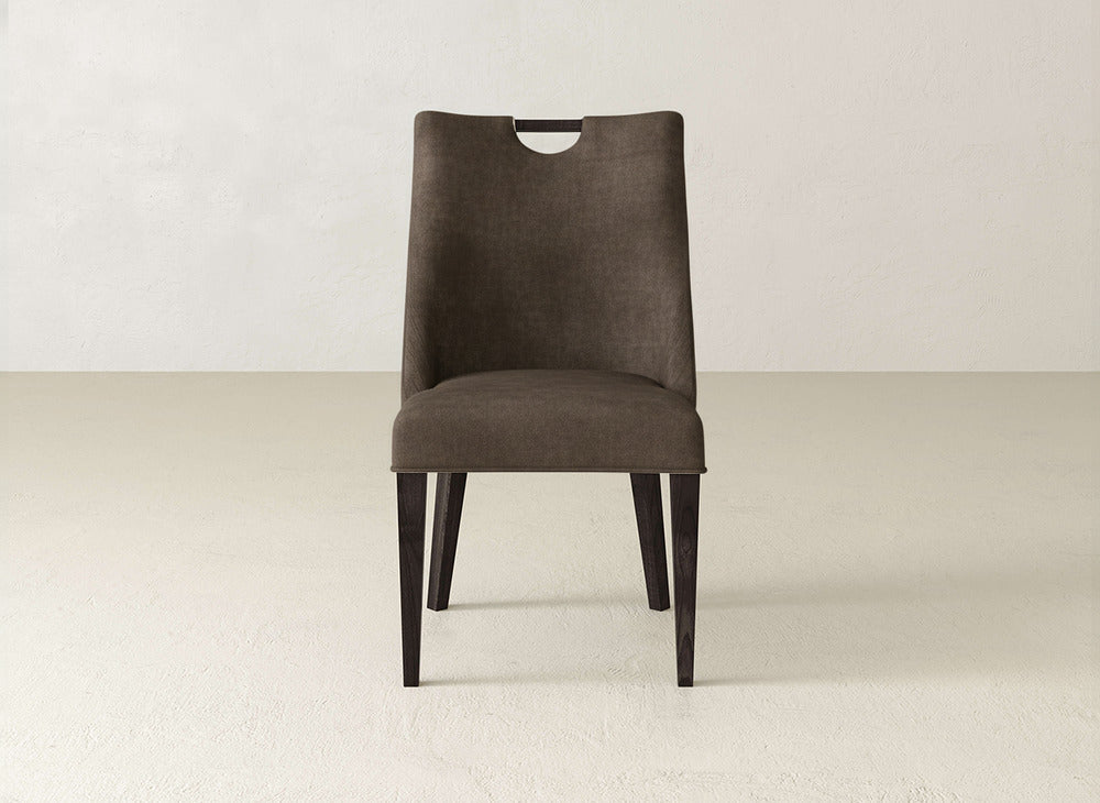 The James & James Rosalie Dining Chair features a modern brown upholstered seat, dark wood legs, and a sleek cutout handle for added style in any light-colored room.
