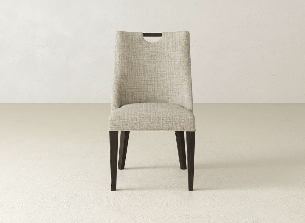 The James & James Rosalie Dining Chair showcases beige upholstery and dark wood legs, displayed front-facing in a minimal, light room with plain walls and floor—a stylish modern choice for contemporary dining spaces.