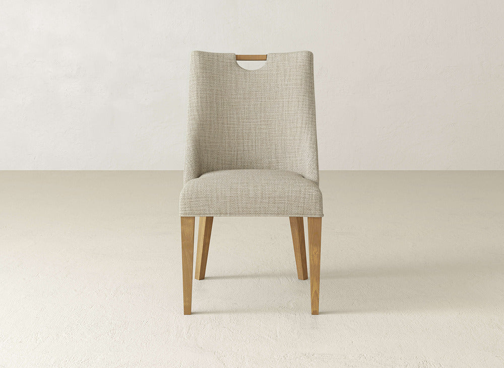 The James & James Rosalie Dining Chair has beige textured upholstery, wooden legs, and a cutout handle at the back—modern style perfect for neutral floors and light walls.