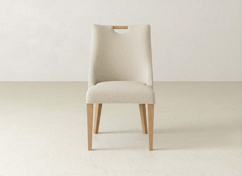 The James & James Rosalie Dining Chair showcases light wood legs and a textured, light beige upholstered seat and backrest, offering an elegant silhouette ideal for dining spaces.