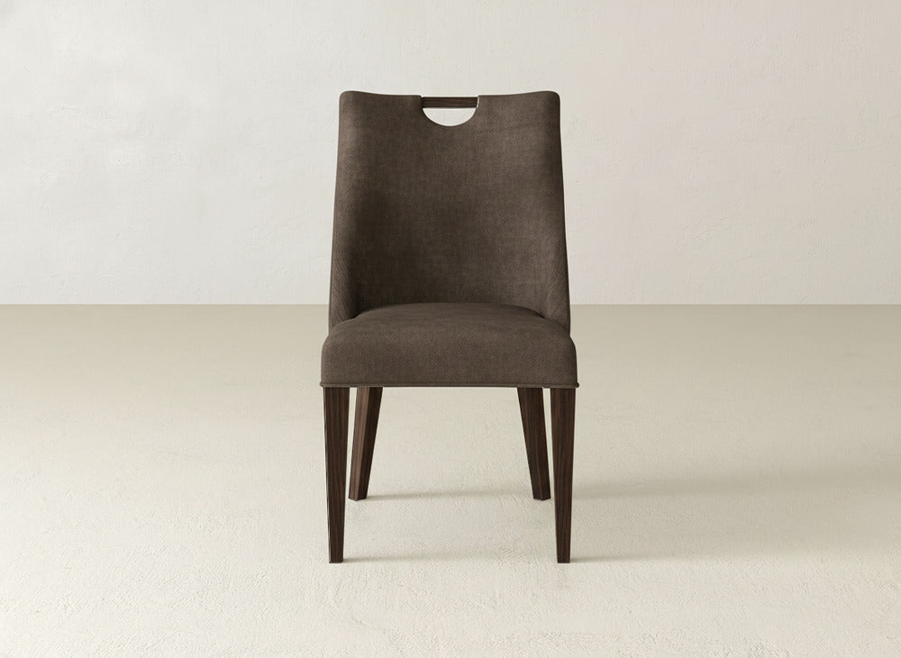 The Rosalie Dining Chair by James & James features a curved backrest, dark brown upholstery, and tapered wooden legs, set on a light floor against an off-white wall.