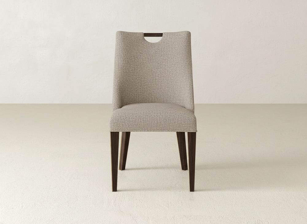 The James & James Rosalie Dining Chair features textured light gray upholstery, dark wooden legs, and a sleek wooden handle cutout—an ideal modern addition to any minimal, neutral-toned space.