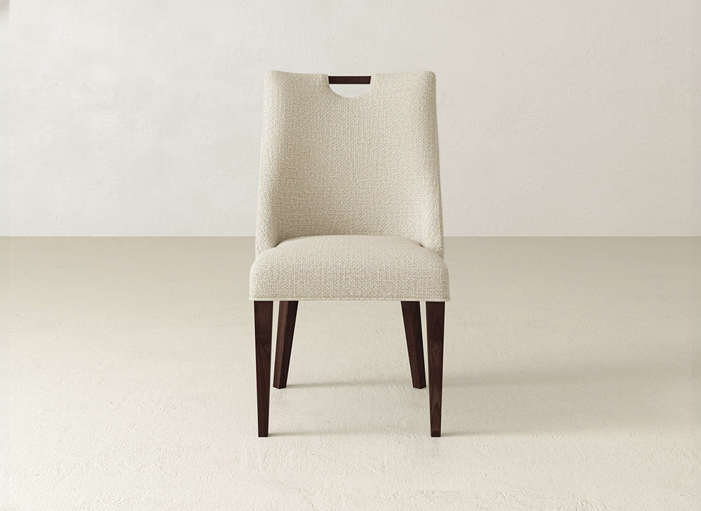 The Rosalie Dining Chair by James & James features modern upholstery in light beige fabric and dark wooden legs, shown on a light floor with a plain, light wall backdrop.