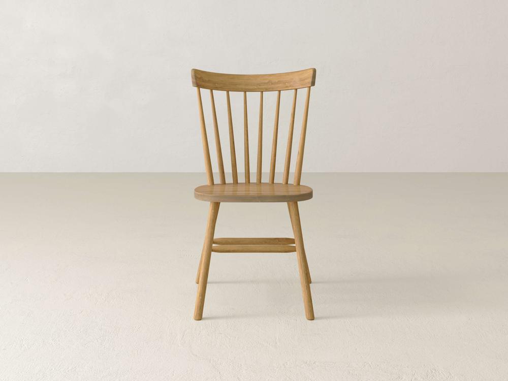Wooden chair with vertical spindle backrest and simple design, placed against a plain white backdrop on a light-colored floor.