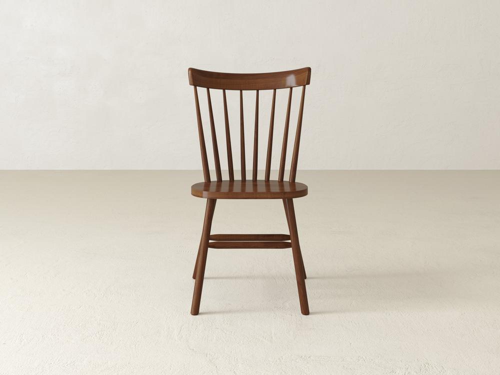 Wooden chair with vertical spindle backrest and simple design, placed against a plain white backdrop on a light-colored floor.
