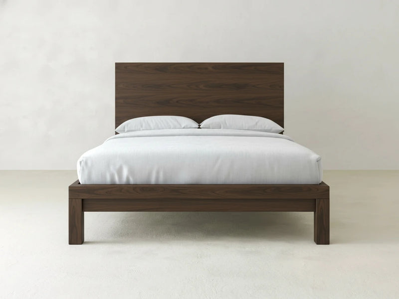 The Sawyer Bed - Sable on Oak by James+James features a modern wooden frame with a tall headboard, white bedding, and two pillows, set against a plain white background.