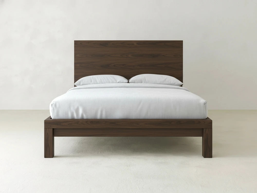 The Sawyer Bed - Sable on Oak by James+James features a modern wooden frame with a tall headboard, white bedding, and two pillows, set against a plain white background.