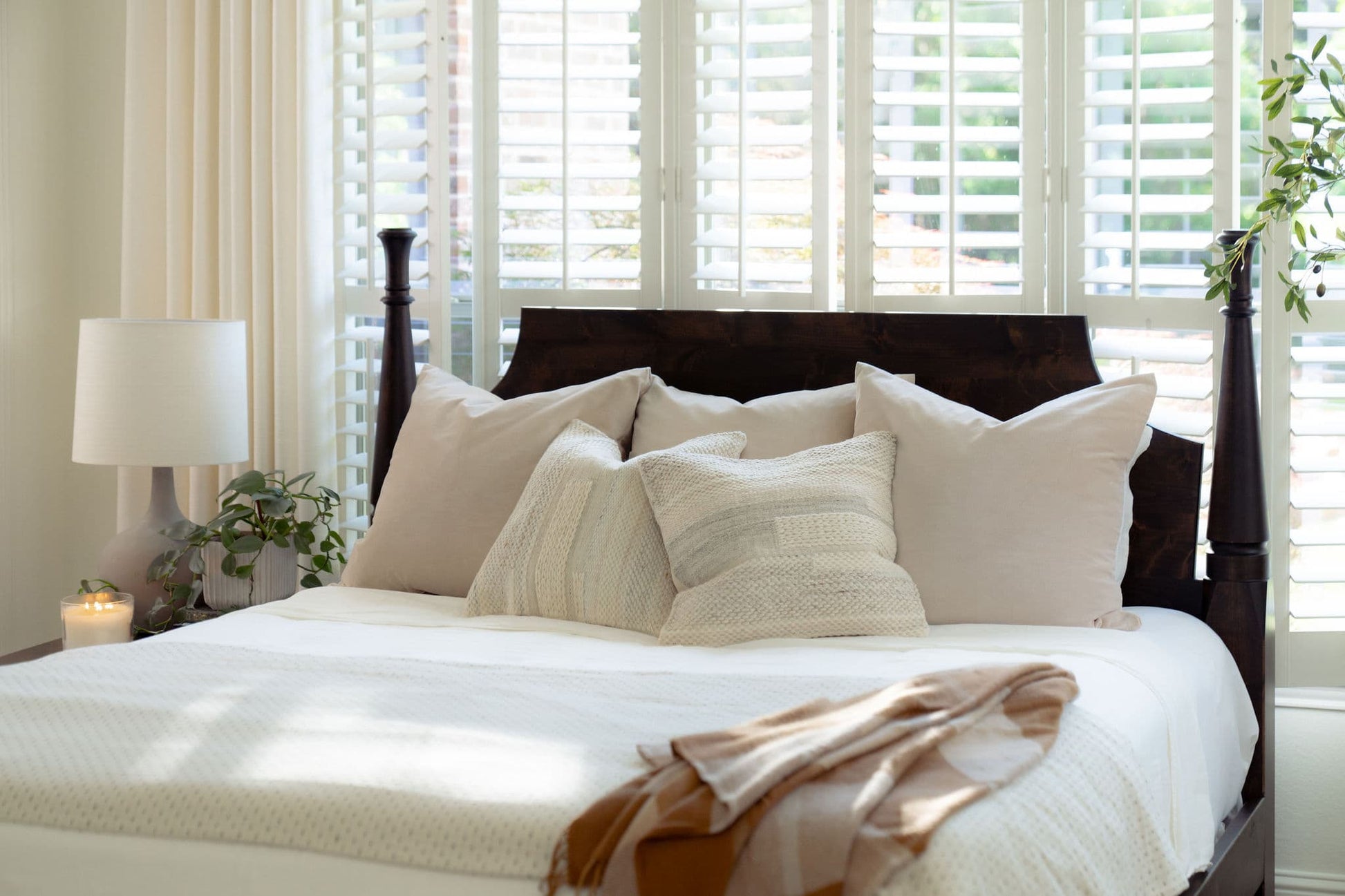 Bedroom with a bed featuring pillows and a blanket, next to a lamp and window blinds.