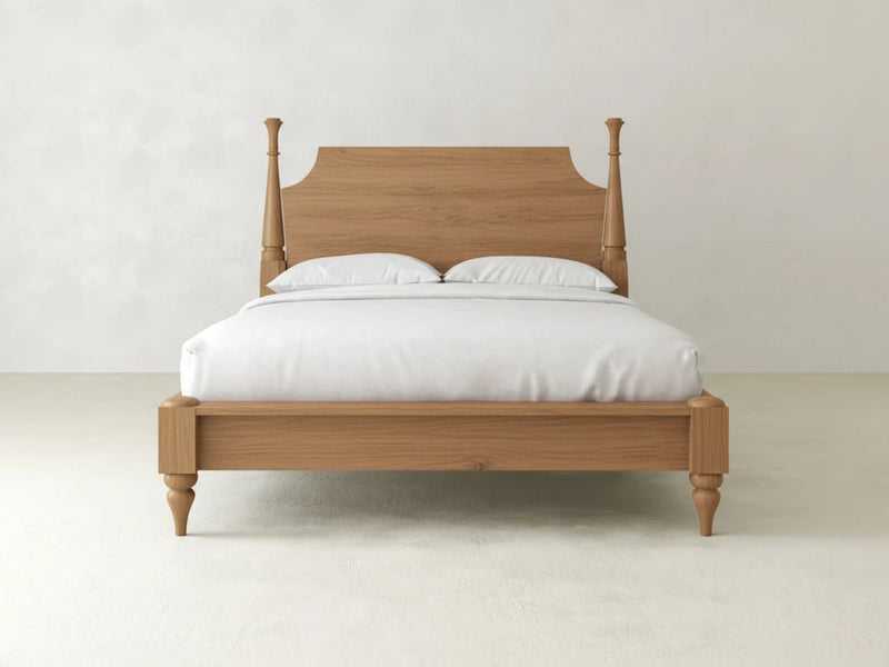 The Stella Bed - Oat on Oak by James+James, featuring a headboard and dressed in white bedding with two pillows, is centrally placed in a minimal, light-toned room with plain walls and flooring.