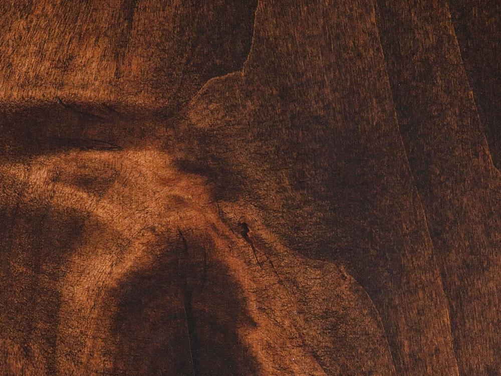 Close-up of the textured surface of the Rae Coffee Table - Tobacco by James+James, showcasing an abstract pattern with various shades of brown. The wood grain creates natural lines and swirls, adding depth and visual interest to the image.