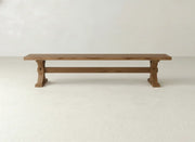 The James+James Trestle Bench - Oat on Oak features a long, rectangular oak design with sturdy legs and minimalist style, set against a plain white wall on a light-colored floor.