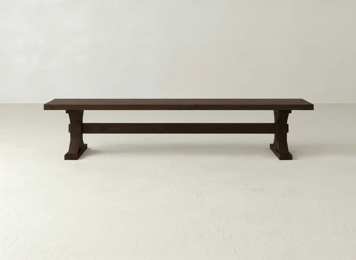 The Trestle Bench - Sable on Oak by James+James features a long, dark wooden seat with sturdy, simple legs, set against a plain, light-colored wall and floor.