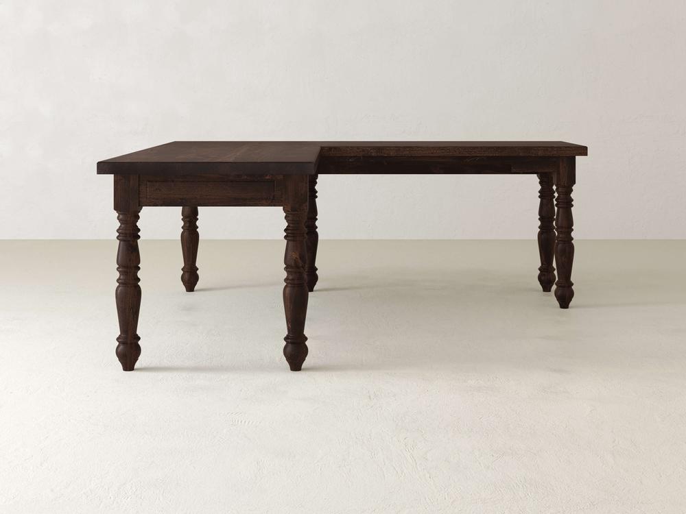 The Turned Leg Corner Desk - Tobacco by James+James is a wooden L-shaped table with a dark, polished finish, set against an off-white background. It features intricately carved legs that highlight its classic design.