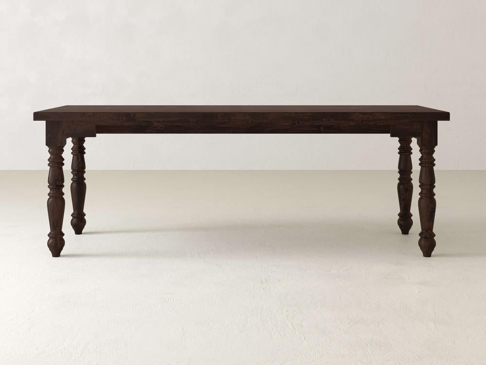 The Turned Leg Desk - Tobacco by James+James, featuring a dark wooden surface and intricate turned legs, stands out against a simple light-colored backdrop.