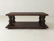 The Vivien Coffee Table by James+James, with its rectangular shape and rich tobacco-colored wooden finish, is elegantly supported by four thick, intricately carved legs. It boasts an additional lower shelf and stands out beautifully against a plain, light-colored background.